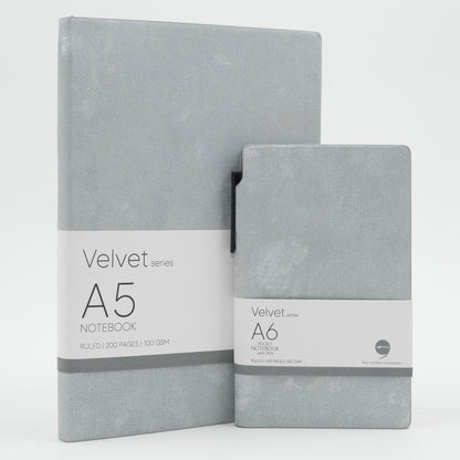 A set of two grey velvet notebooks, one A5 size and one A6 size, with a grey ballpoint pen and labeled 'Velvet Series A5' and 'Velvet Series A6' respectively.