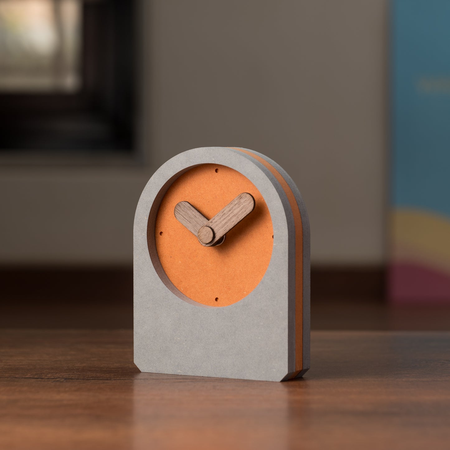 A square-shaped table clock with an orange front and gray back, featuring wooden hands and a digital display.