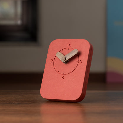 A rectangular red table clock with a wooden stand and clock hands, displaying the time.