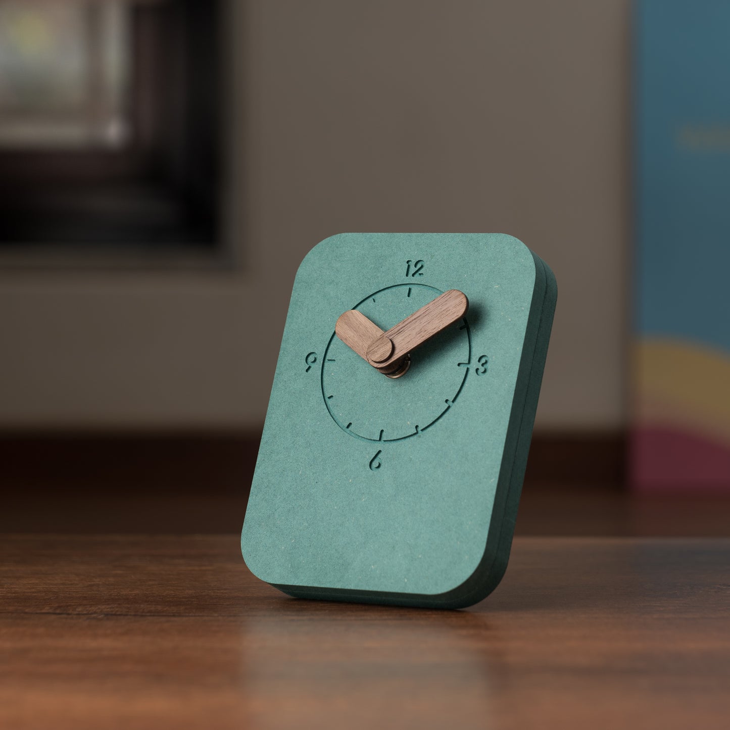 A rectangular green table clock with a wooden stand and hands, displaying the time.