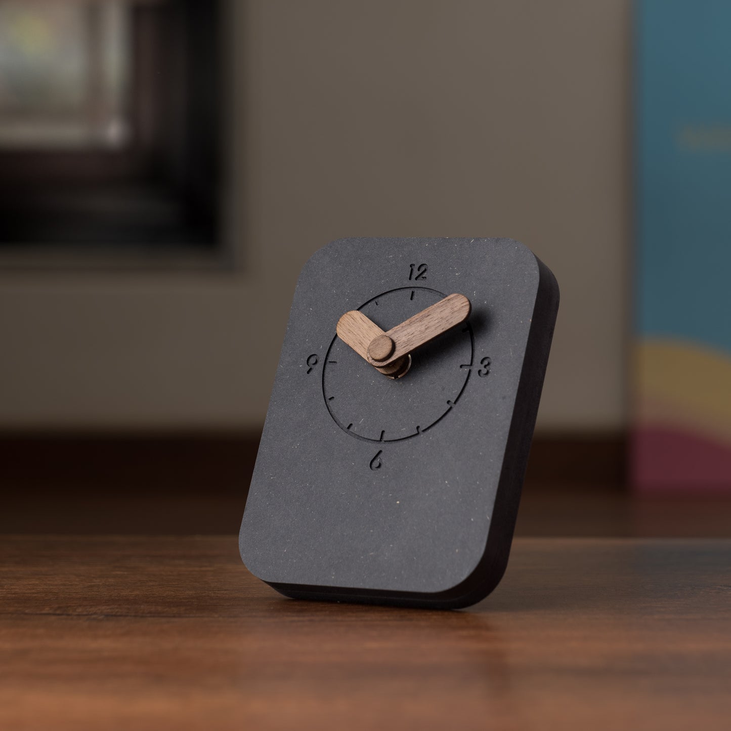 A black, rectangular table clock with a wooden stand and hands, displaying the time.
