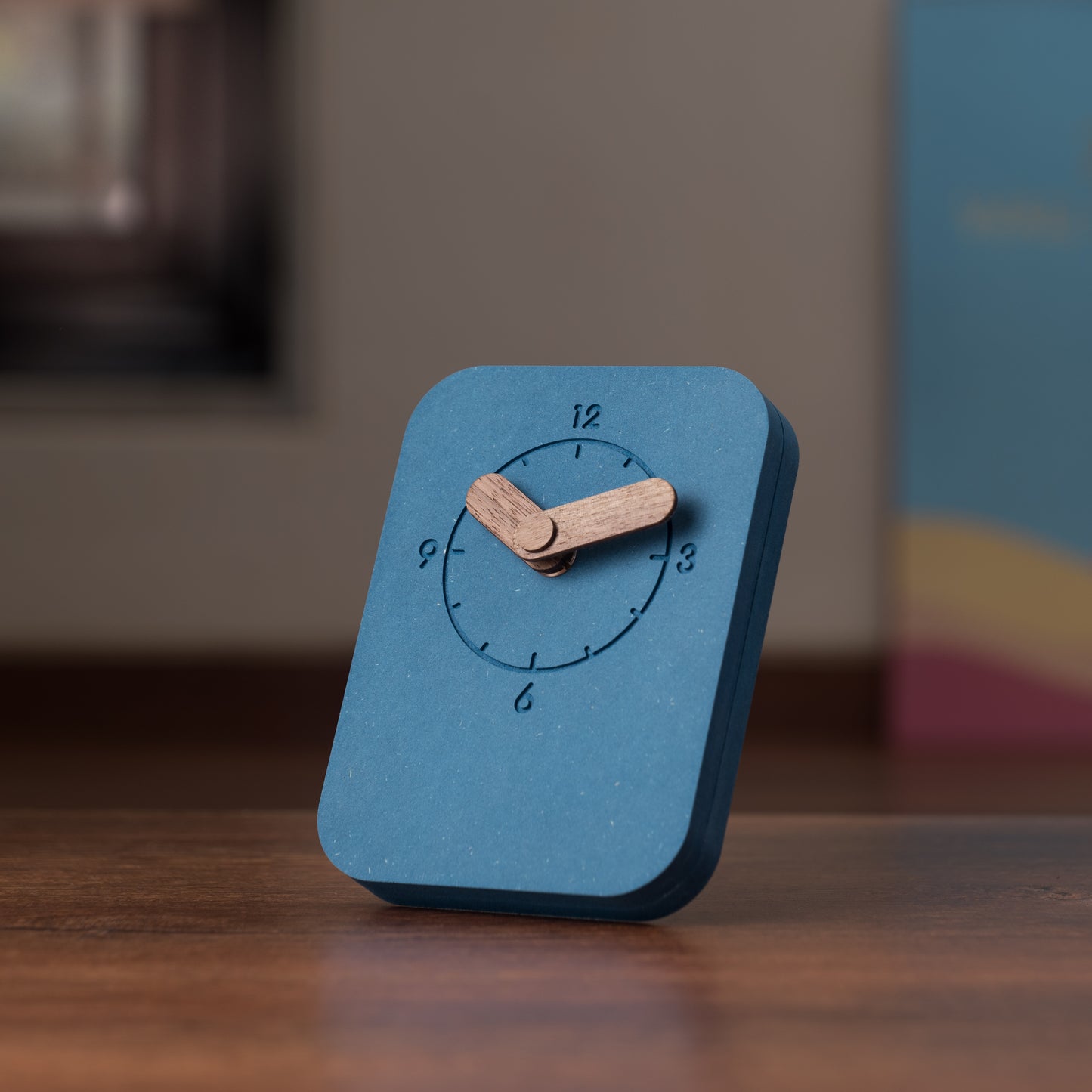 A blue rectangular table clock with a wooden stand and hands, displaying the time.
